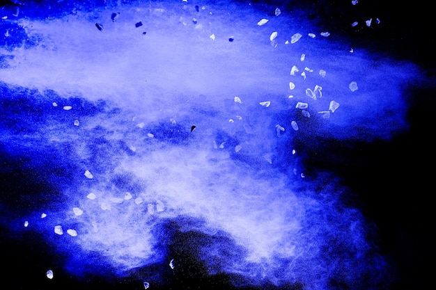 Detriti spaccati di pietra che esplodono con polvere blu su sfondo nero