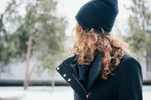 Dettagli dell&#39;abbigliamento femminile: ragazza con i capelli ricci in un cappotto nero e cappuccio primo piano all&#39;aperto nel parco