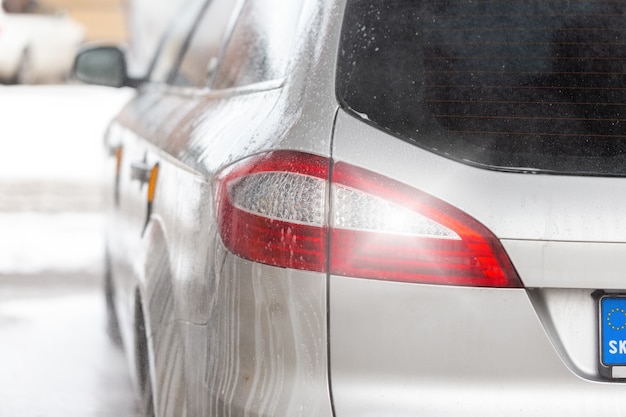 Dettaglio del fanale posteriore di un'auto moderna argentata all'interno dell'autolavaggio con gocciolamento di sapone