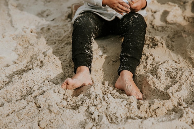 Dettaglio delle gambe delle ragazze con i piedi sporchi dall'ubicazione della sabbia e scavando nella sabbia durante la soleggiata giornata estiva