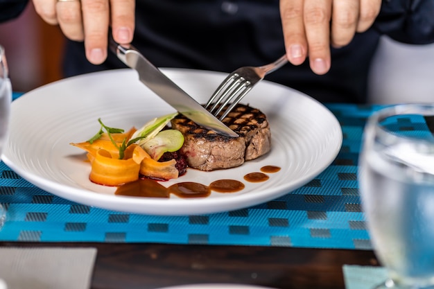 Dettaglio delle mani di una persona che taglia un filetto di carne guarnire con verdure con forchette in un ristorante.