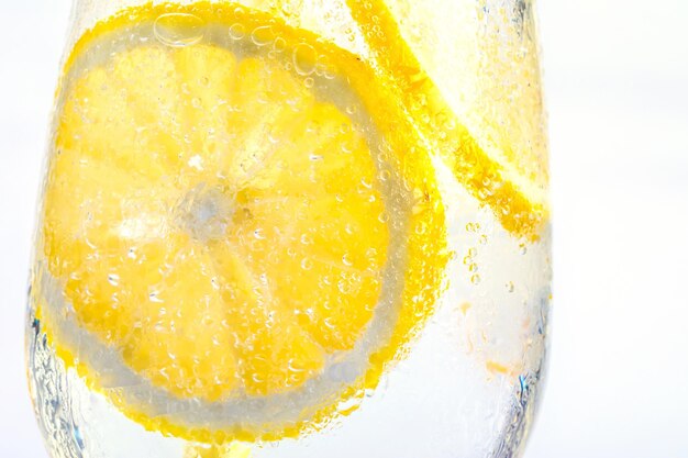 Dettaglio di acqua gassata con fette di limone nel bicchiere isolato su sfondo bianco