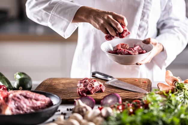 Dettaglio di pezzi di carne rossa messi in una ciotola bianca su un tavolo di preparazione dei pasti pieno di ingredienti.