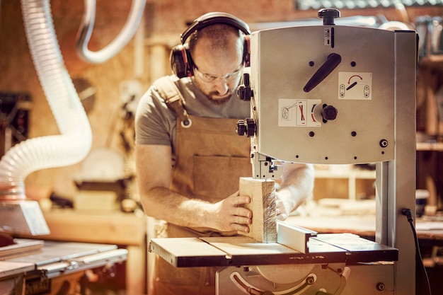 Dettaglio di un falegname al lavoro tagliando una tavola con una sega a nastro nel suo laboratorio