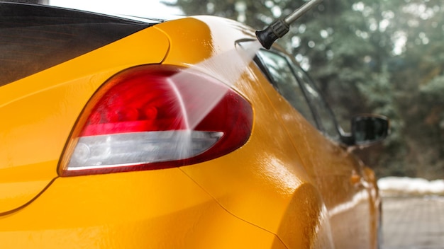 Dettaglio sulla luce posteriore gialla dell'auto lavata nell'autolavaggio self-service, getto d'acqua a spruzzo.