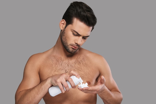 Devo radermi. Bel giovane che applica crema da barba mentre sta in piedi su sfondo grigio gray