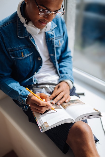 Devo verificare. Studente serio dalla pelle scura che china la testa mentre guarda il suo libro