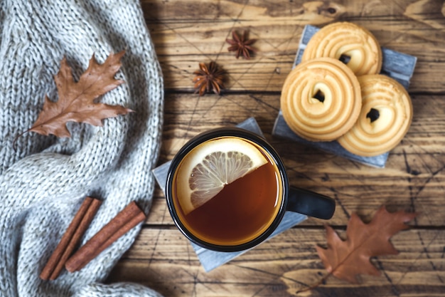 Di autunno vita ancora con la tazza di tè, biscotti, maglione e foglie sulla superficie in legno.