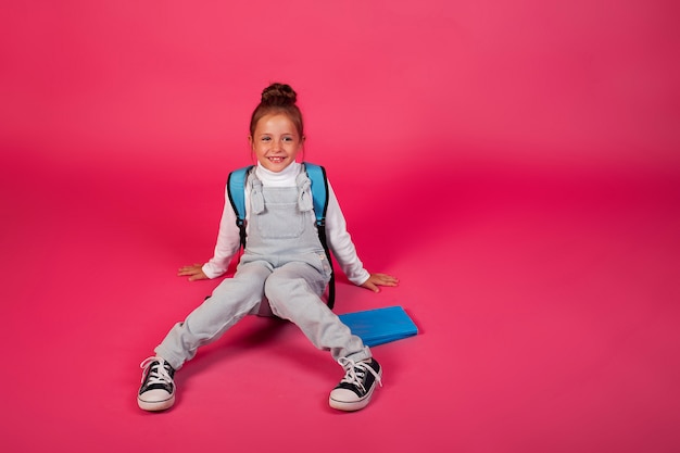 Di nuovo a scuola. allegra ragazza felice con uno zaino blu su sfondo rosa.