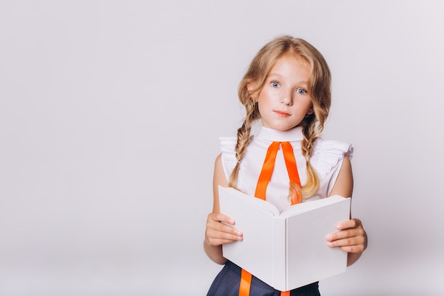 Di nuovo a scuola. Carina adorabile ragazza bionda caucasica con il libro in uniforme scolastica su sfondo bianco