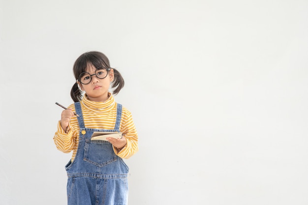 Di nuovo a scuola. Una bambina divertente con gli occhiali su sfondo bianco. Bambino della scuola elementare con un libro. Formazione scolastica