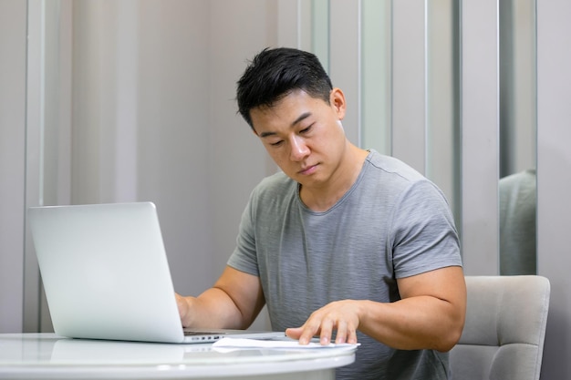 Di un giovane che utilizza un computer portatile e guarda i documenti alla sua scrivania in un comodo soggiorno