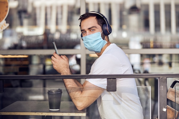 di un uomo in maschera al caffè con lo smartphone in cuffia