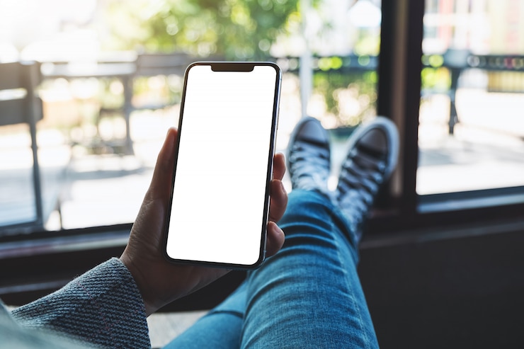 Foto di una donna che tiene il telefono cellulare con lo schermo del desktop bianco bianco mentre era seduto nella caffetteria