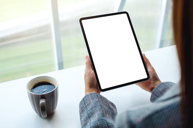 di una donna con tablet pc nero con schermo bianco vuoto con una tazza di caffè sul tavolo