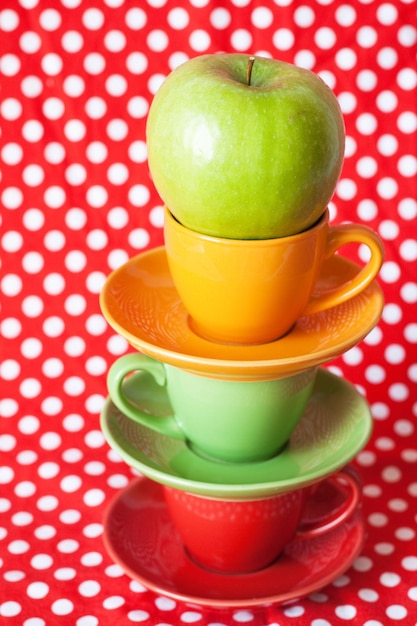 Diapositiva di tazze multicolori e supporto mela verde su sfondo rosso a pois