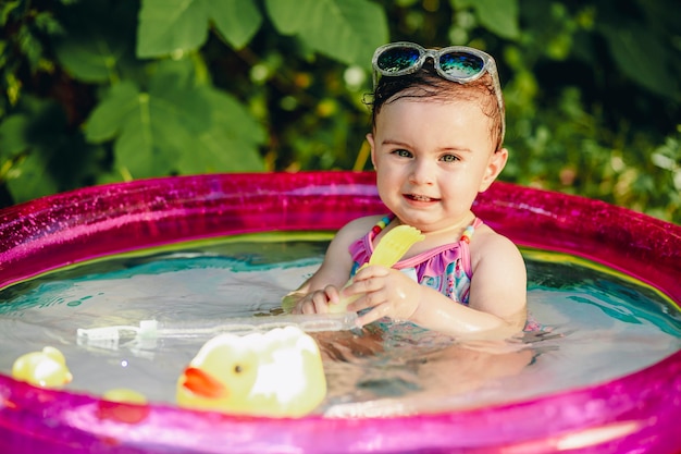 Dieci mesi di età che si gode il calore dell'estate nella sua piscina con i giocattoli di anatra di gomma gialla