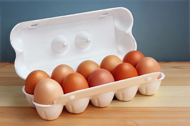 Dieci uova di gallina marrone in un pacchetto di polistirolo bianco sul tavolo di legno.