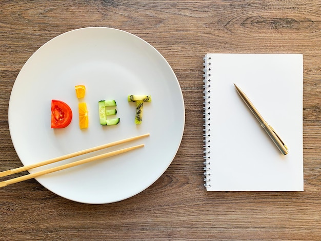 Dieta di parola fatta di verdure affettate in piatto bianco e programma di dieta su fondo di legno