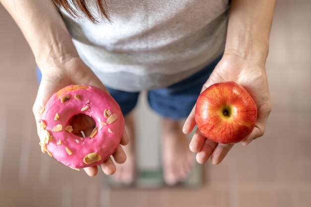 Dieta Dieta giovane donna asiatica o ragazza che misura il corpo che pesa sulla bilancia tenere la ciambella dolce e la mela rossa scegliere mangiare cibo per una buona salute sana quando si ha fame Perdita di peso persona vista dall'alto