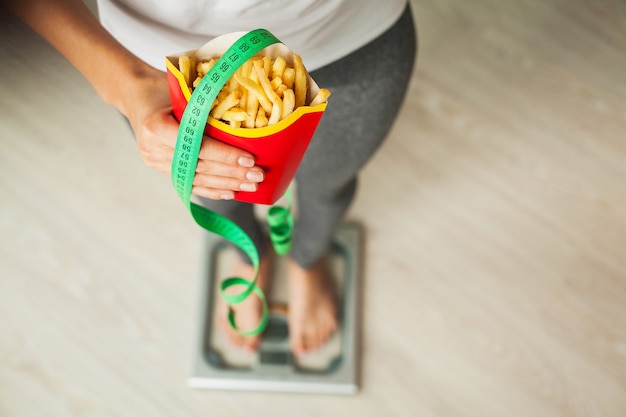 Dieta. Donna in piedi sulle scale e tenendo una patatine fritte.