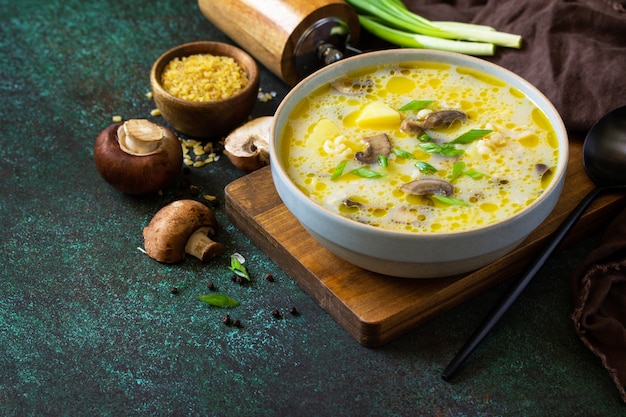 Dieta e concetto di mangiare sano. Zuppa di crema di funghi reale con bulgur su uno sfondo di pietra scura. Copia spazio.