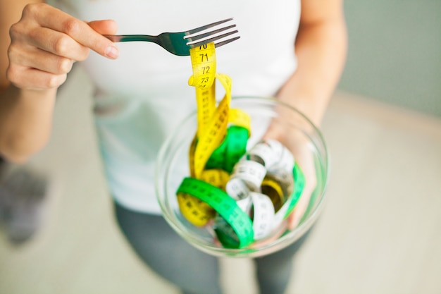 Dieta e perdita di peso. La donna tiene la ciotola e la forchetta con nastro adesivo di misurazione