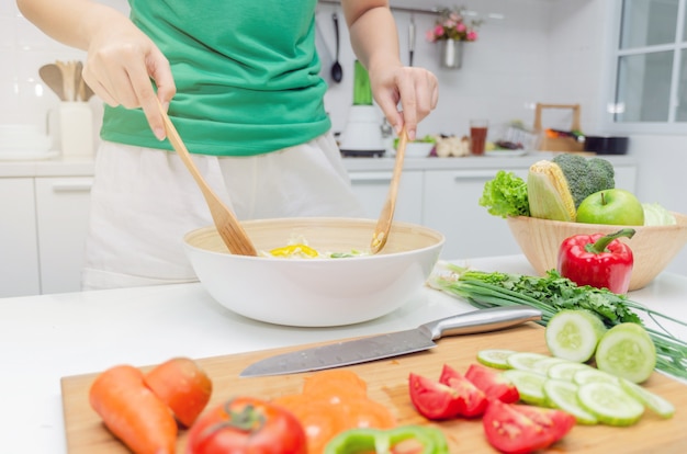 Dieta. giovane donna graziosa in camicia verde in piedi e preparare l'insalata di verdure in una ciotola per il bene sano nella cucina moderna a casa