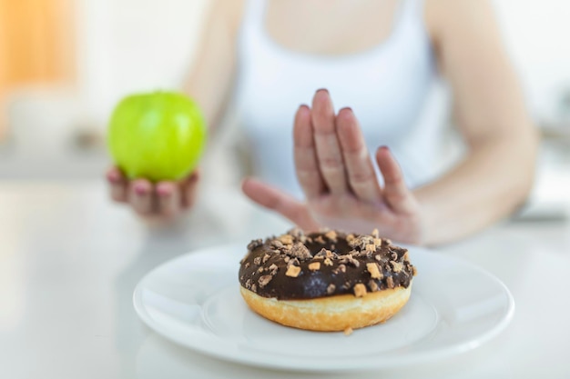 Dieta o concetto di buona salute. Giovane donna che rifiuta cibo spazzatura o cibo malsano come ciambelle o dessert e sceglie cibo sano come frutta o verdura fresca.