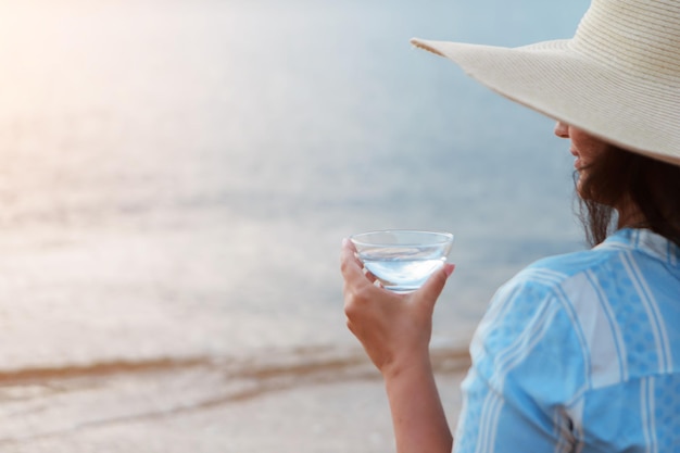 Dieta sana alimentazione e riposo donna beve acqua pulita in vetro di sfondo mare una donna sulla spiaggia e...