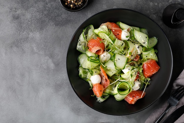 Dieta sana insalata con salmone affettato cetrioli mozzarella microgreens su piastra nera e sfondo grigio