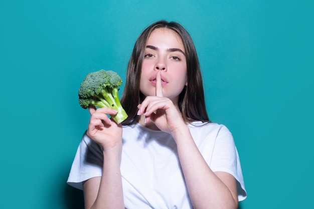 Dieta segreta della donna Vita sana del cibo Ritratto di giovane bella donna che mangia broccoli su sfondo blu