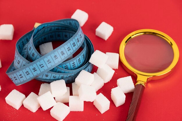Dieta senza zucchero per dimagrire. Una pila di zollette di zucchero bianco e dentro un metro blu. Sfondo rosso. Copia spazio.