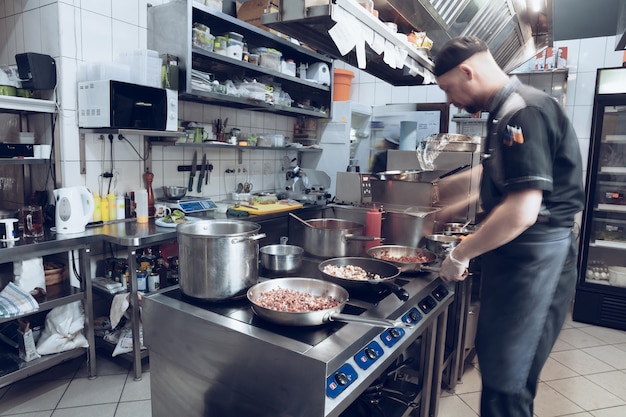 Dietro le quinte dei marchi. Lo chef che cucina in una cucina professionale di un pasto al ristorante per il cliente o la consegna. Aprire gli affari dall'interno. Pasti durante la quarantena. Sbrigati, movimento.