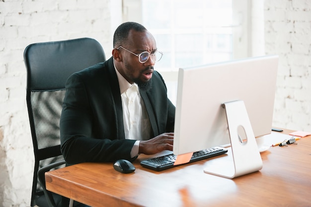 Digitando il testo. Imprenditore afroamericano, uomo d'affari che lavora concentrato in ufficio. Sembra serio e impegnato, indossa un abito classico, una giacca.