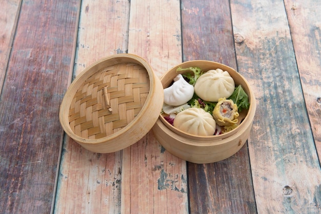 Dim sum cinese assortito all'interno di una ciotola di legno per la cottura a vapore farcita con gamberi e carne di maiale su tavola di legno