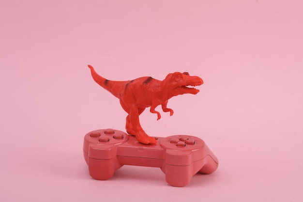 Dinosauro giocattolo Tyrannosaurus rex con gamepad su sfondo rosa Minimalismo layout creativo