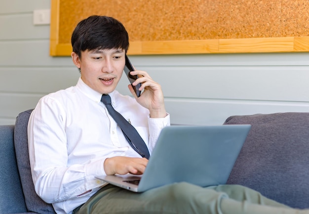 Dipendente asiatico premuroso giovane uomo d'affari di successo professionale bello in abito formale di affari seduto su un divano accogliente divano pensando idee lavorando con il computer portatile in soggiorno.