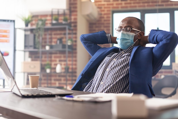 Dipendente che si rilassa alla scrivania dopo aver terminato l'attività di progetto aziendale durante la pandemia. Imprenditore calmo che si prende una pausa per rilassarsi dopo il lavoro e portare a termine il lavoro. Uomo seduto con le mani sopra la testa.