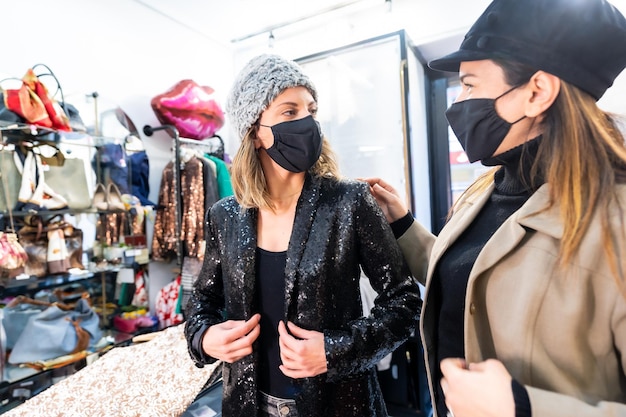 Dipendente e cliente con maschere in un negozio di abbigliamento di lusso, misure di sicurezza nella pandemia di coronavirus, covid-19