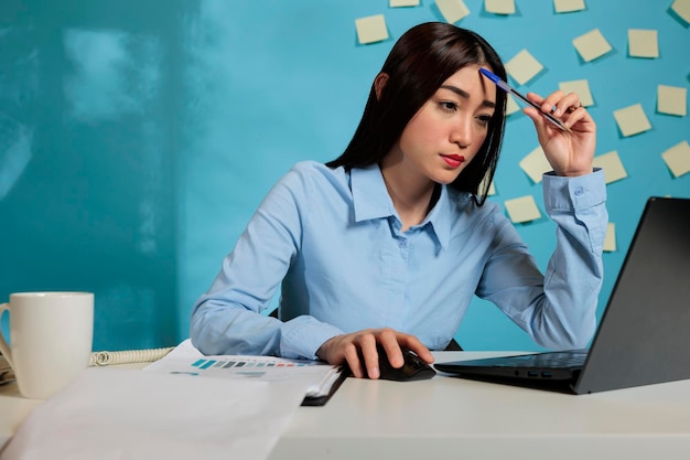 Dipendente femminile dell'azienda che fa brainstorming per progettare una nuova strategia di pianificazione del progetto. La donna si è concentrata sullo sviluppo di procedure di lavoro efficaci seduti alla scrivania dell'ufficio con il computer portatile.