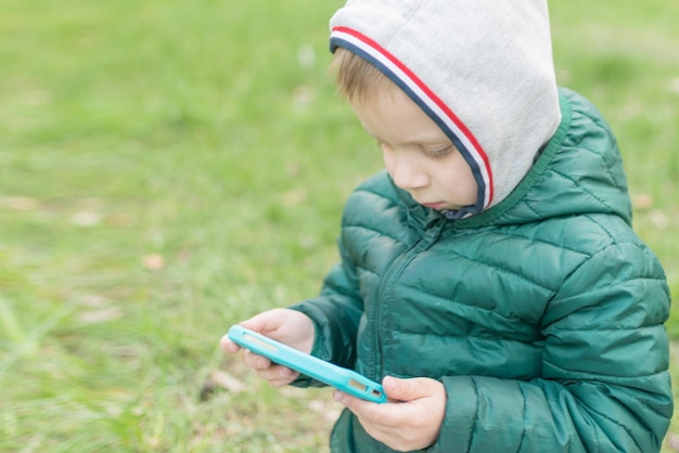 Dipendenza dei bambini dai telefoni cellulari Il ragazzino sta giocando con il telefono per strada