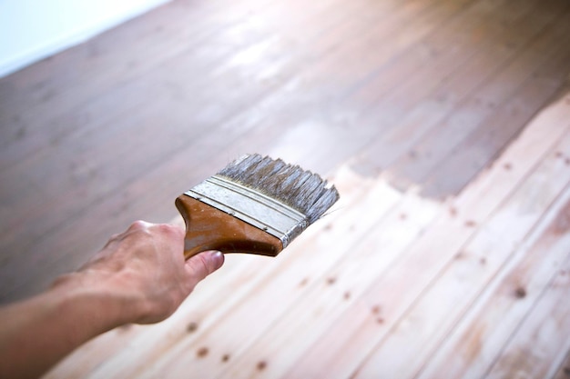 Dipingere a mano un pavimento in legno con un pennello