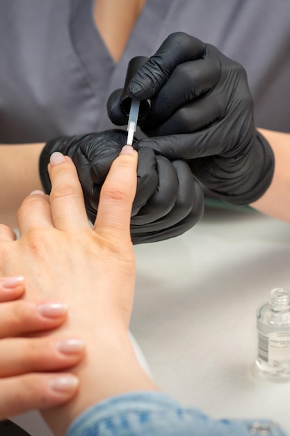 Dipingere le unghie femminili. Mani di manicure in guanti neri sta applicando smalto trasparente sulle unghie femminili in un salone di manicure.