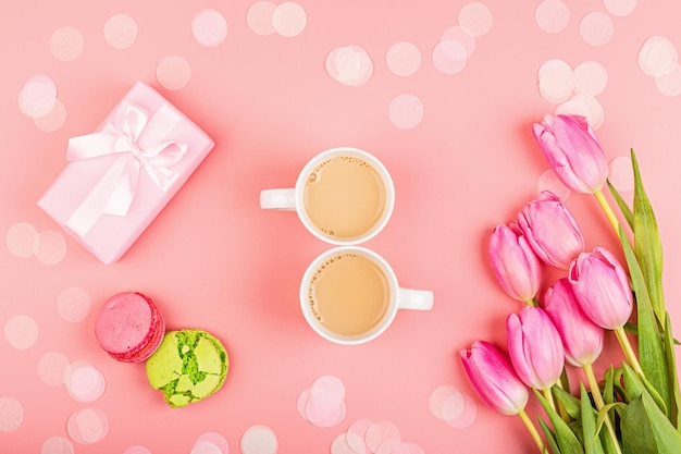 Directamente sopra la foto di una tazza di caffè e un macarrone con un regalo e un bouquet su uno sfondo rosa