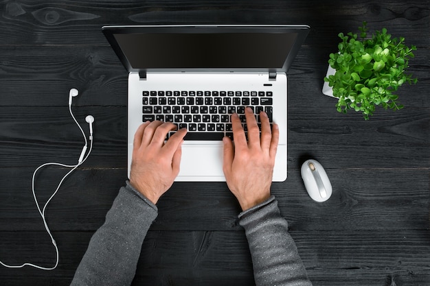 Direttamente sopra la vista delle mani umane che digitano sul laptop. Computer portatile, tablet digitale e pianta in vaso sulla scrivania. Uomo che lavora da casa.