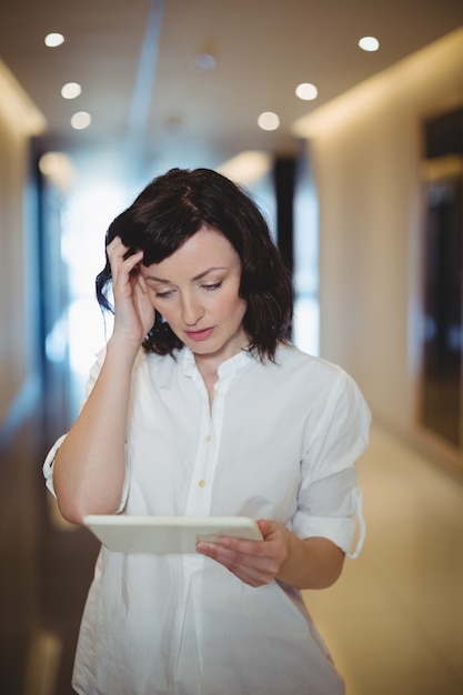 Dirigente femminile utilizzando la tavoletta digitale nel corridoio