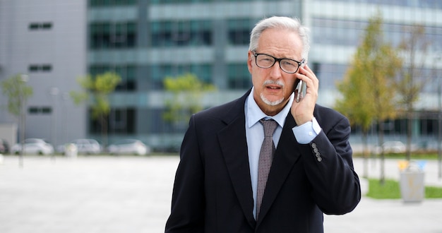 Dirigente senior sulla camminata del telefono all'aperto