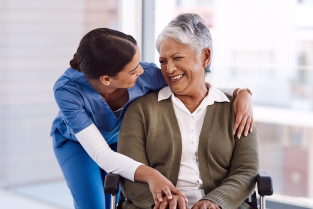 Disabilità sanitaria e un'infermiera che abbraccia una donna anziana su una sedia a rotelle durante una visita a una casa di cura Abbraccio medico e divertente con una professionista della medicina che ride parlando con un residente anziano