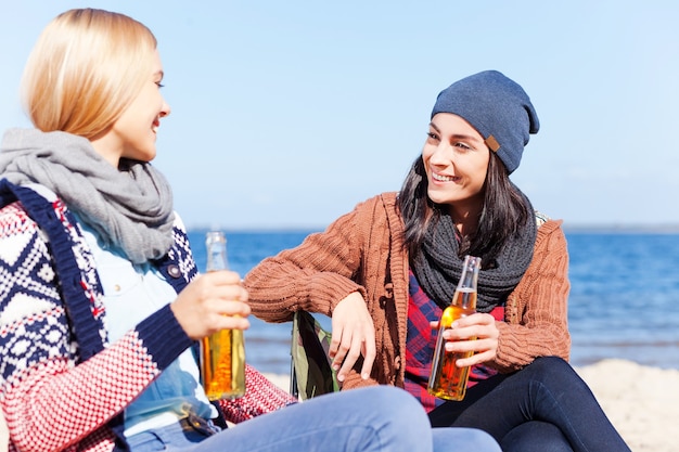 Discorso amichevole. Due belle giovani donne che bevono birra e parlano tra loro seduti insieme sulla spiaggia